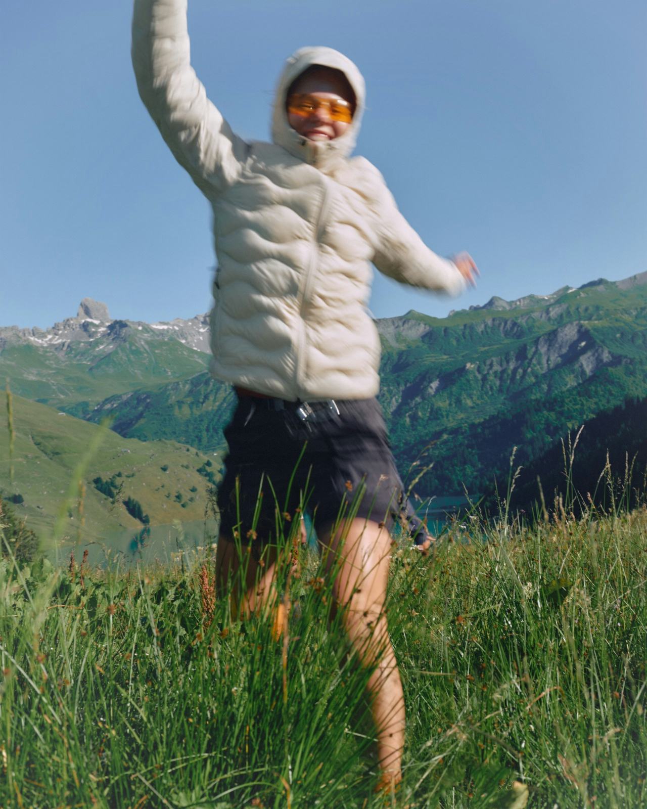 Matchu Matcha Image of Person in a white puffer jacket and shorts standing in a grassy field with mountains in the background