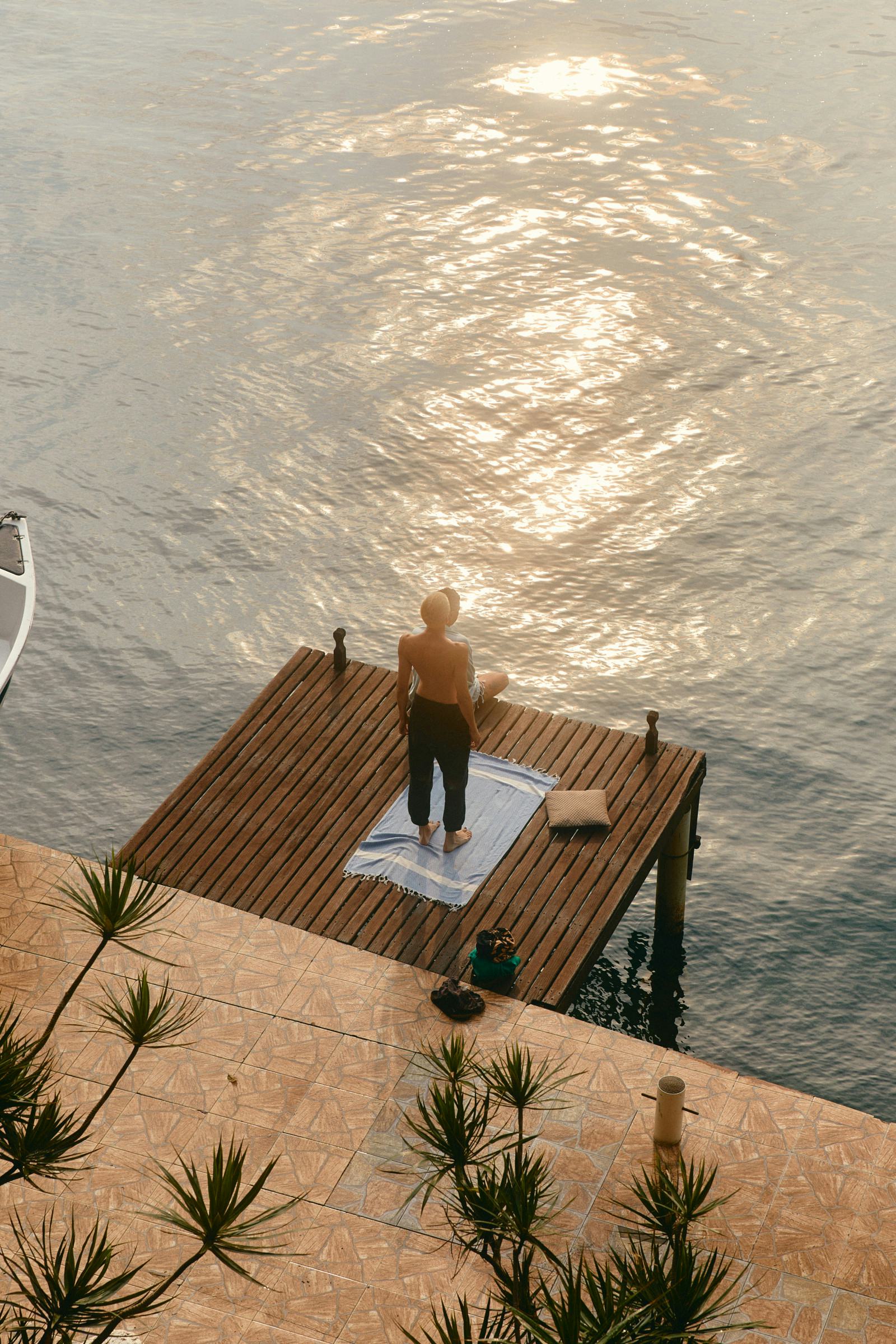 Matchu Matcha Image of Man standing on a wooden dock by the water with a sunset reflection.
