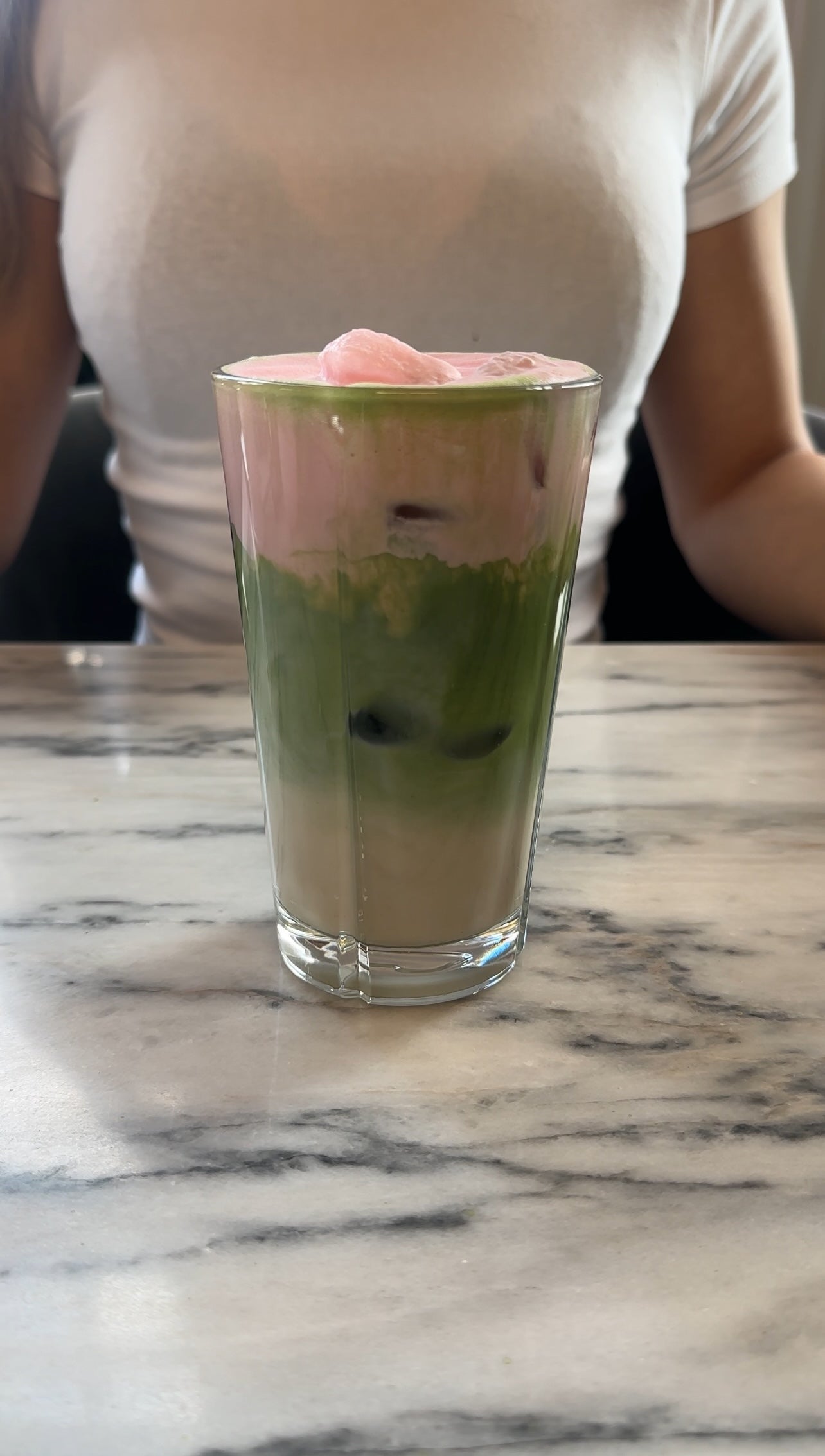 Glass with layered Matchu Matcha dessert on a marble surface
