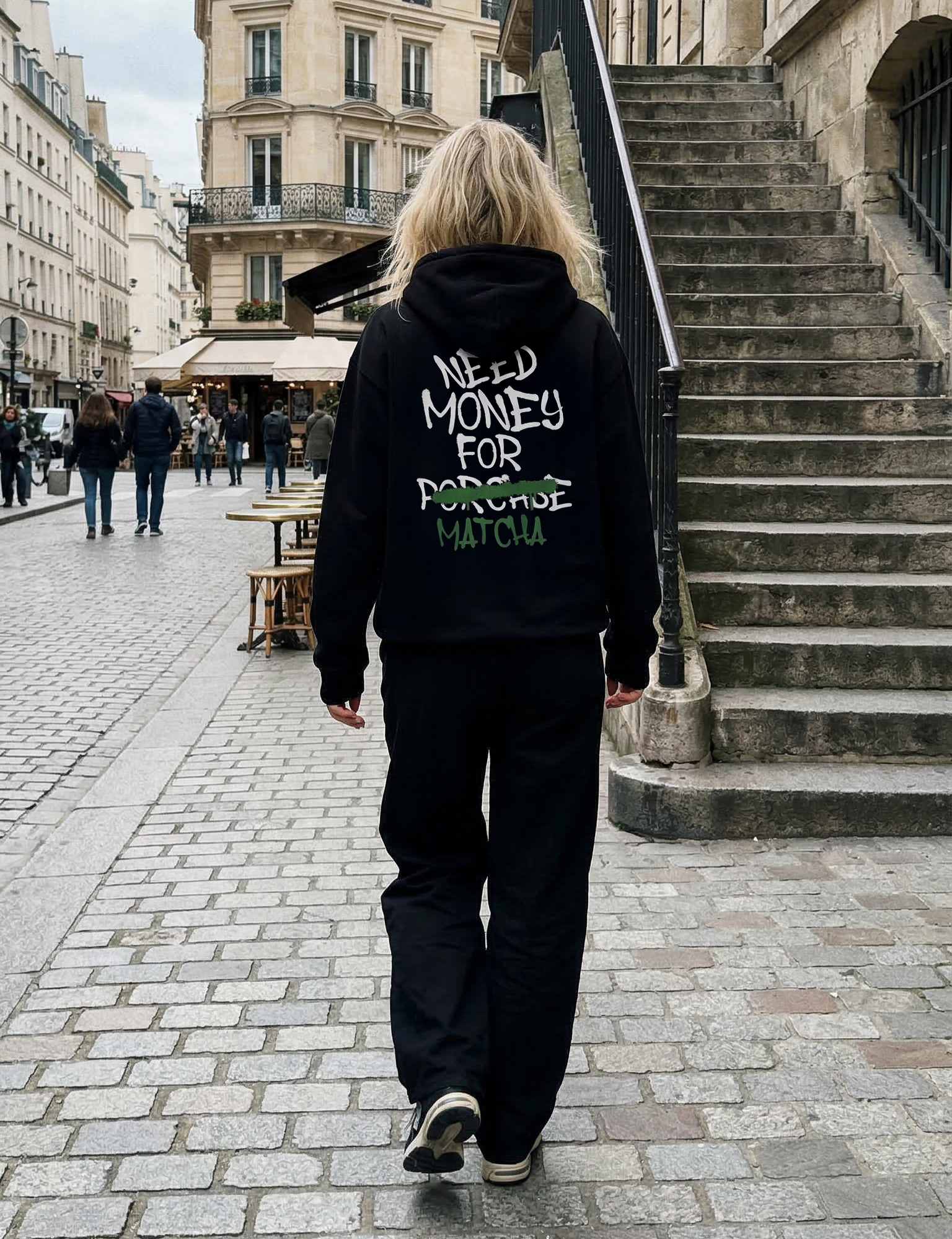 Person wearing a black hoodie with text walking on a city street.